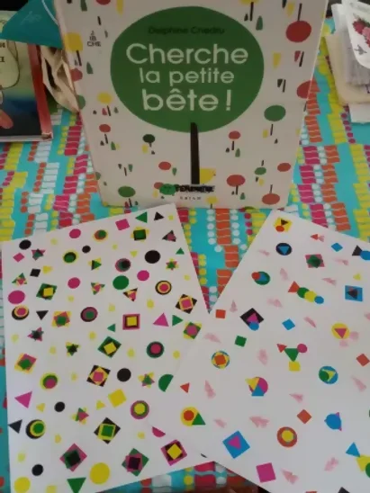 On voit le rendu de l'atelier de cherche la petite bête, deux pages colorées où il faut trouver les éléments cachés. Derrière, le livre de Delphine Chedru "cherche la petite bête" est en exposition