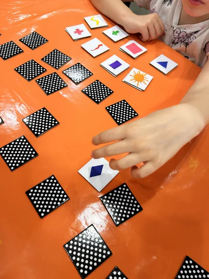Un enfant joue avec le memory des formes réalisé. Les cartes tournées sont noires à pois blancs.