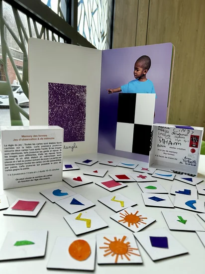 On voit les cartes de memory (soleil, carré, note de musique, losange, escalier, triangle, rectangle, flèche, etc) la boîte de jeu est derrière avec l'album de Claire Dé.
