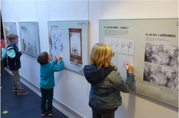 Les panneaux d'exposition de Billy Symphony sont accrochés aux murs. Trois enfants sont en train de jouer sur les versions couvertes de filmes veleda.