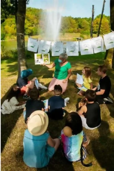 Lecture de l'album de Hugo et Cagoule, on est dans l'herbe, les enfants sont assis. Derrière la lectrice un fil est tendu avec des plaches de la BD.