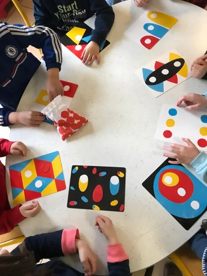 On voit un groupe d'enfants, avec seulement leurs mains visibles, en train de jouer avec le jeu de société issu des albums d'Hervé Tullet.