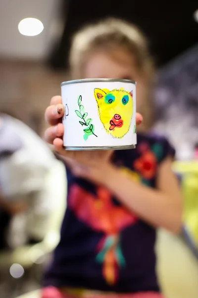 un enfant montre une boîte de conserve décorée d'une étiquette décalée en encre de Chine.
