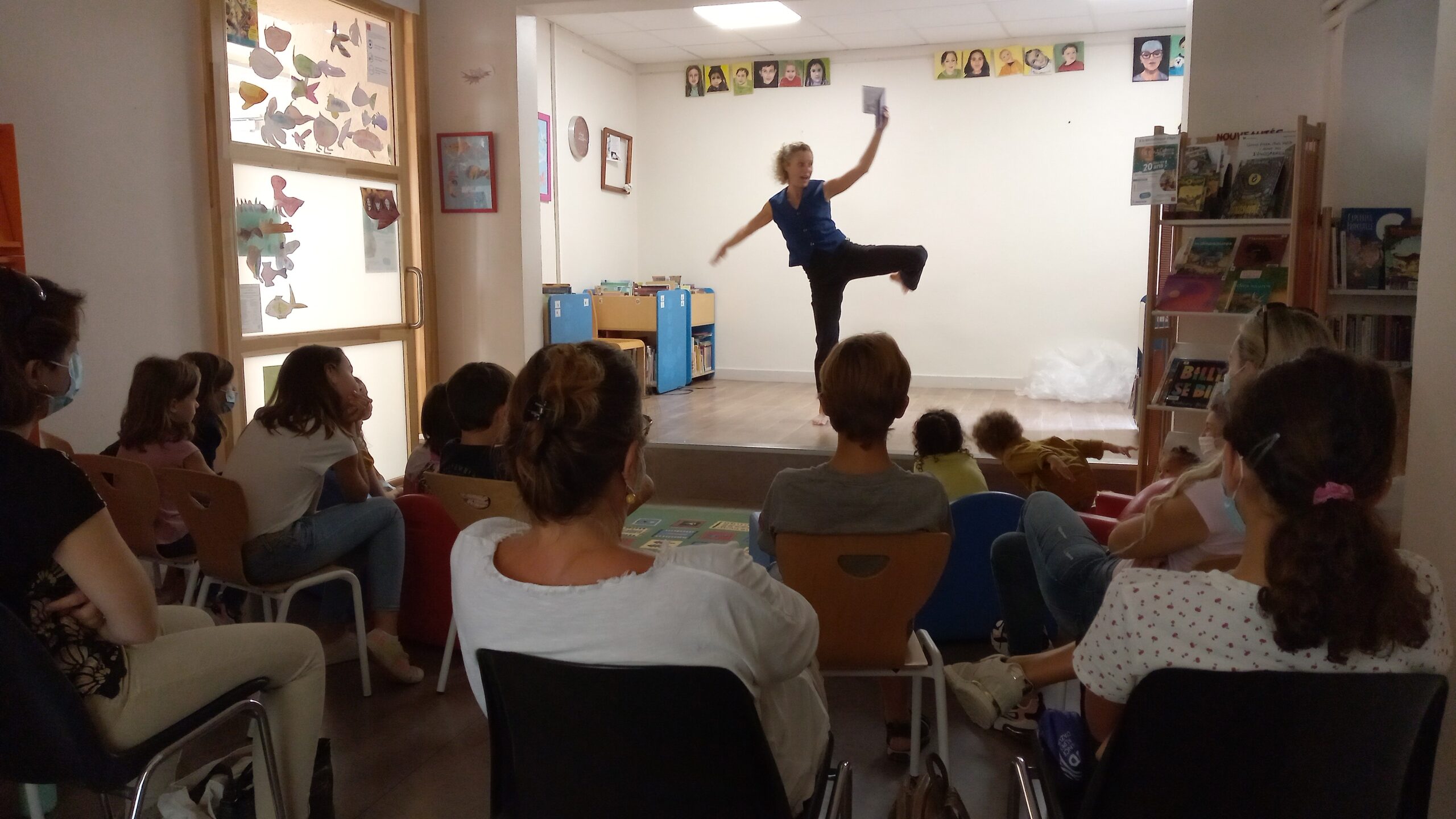 Une danseuse avec un livre à la main danse sur une petite scène devant un public que l'on voit de dos