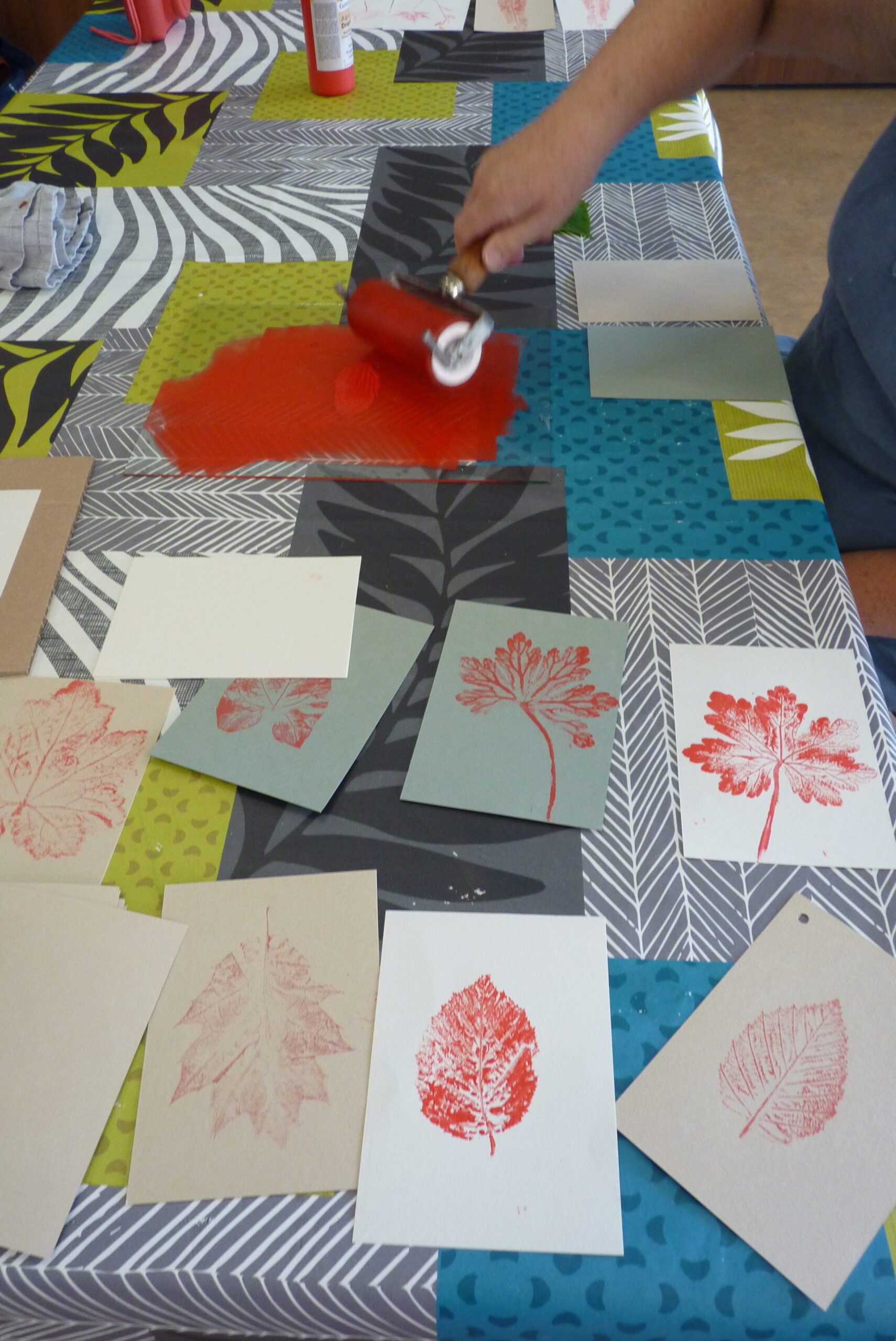 Atelier Perluette "Cueillette en liberté" : un enfant réalise une empreinte végétale à la peinture d'une feuille d'arbre en la pressant à l'aide d'un rouleau.