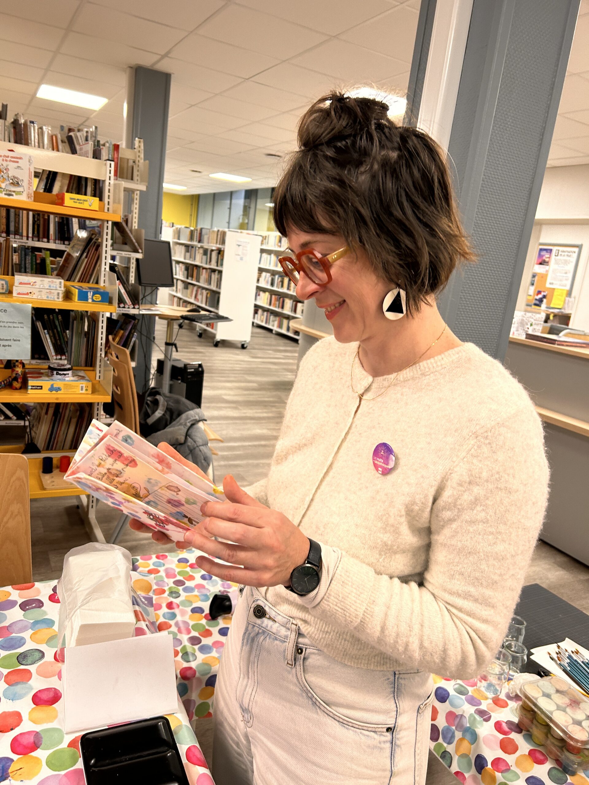 L'illustratrice Magali Dulain regarde le petit livre réalisé par un enfant lors d'un atelier qu'elle vient de mener avec Perluette. Elle sourit.