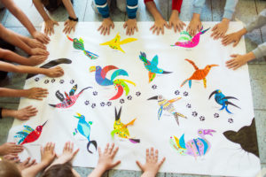 Une des fresques sur les oiseaux. Les enfants ont dessiné des oiseaux de toutes les couleurs. Les mains des enfants tiennent le dessin à plat.