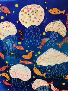 Sur fond bleu marine, des poissons rouges et jaunes et des méduses en assiettes cartons blanches à pois rouges et jaunes eux aussi sont collés afin d'imiter les fonds marins.